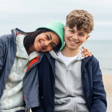 Two teenage friends wearing casual clothing sitting on a wall on a promenade by the sea